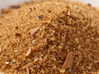 Pile of granular coconut sugar with scattered coconut flakes.